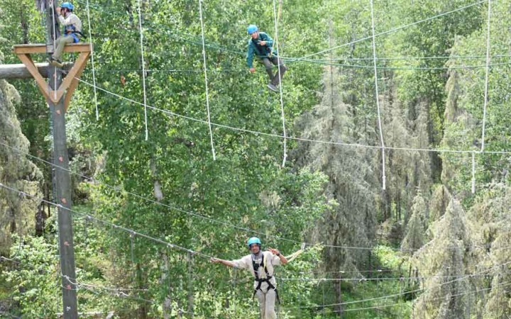 two students are suspended by ropes as they make their way through a ropes course on an outward bound course